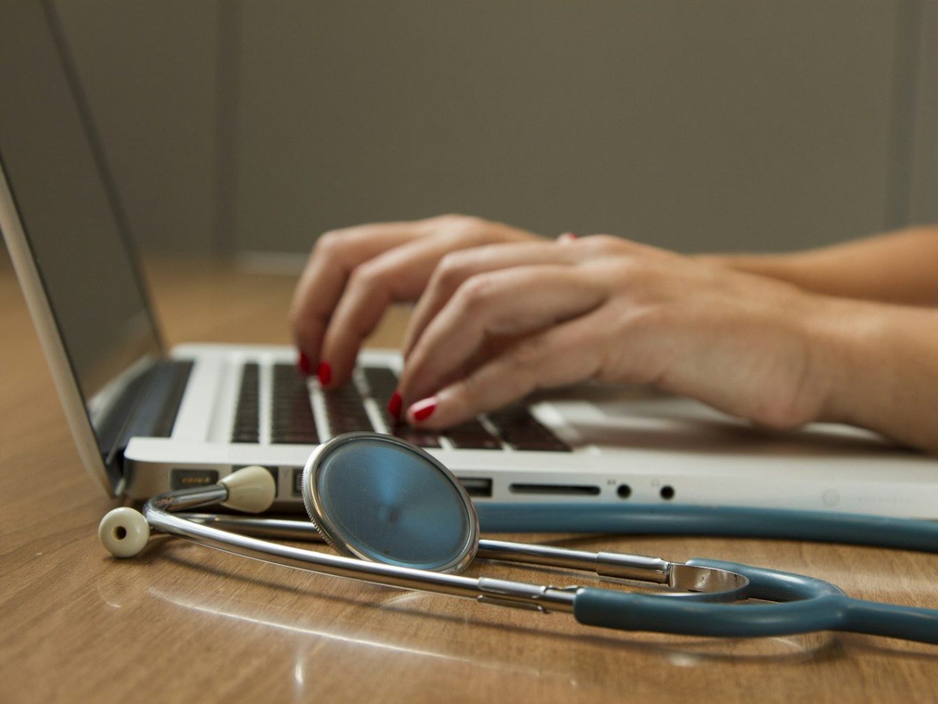 Doctor typing on a laptop with a stethoscope nearby.