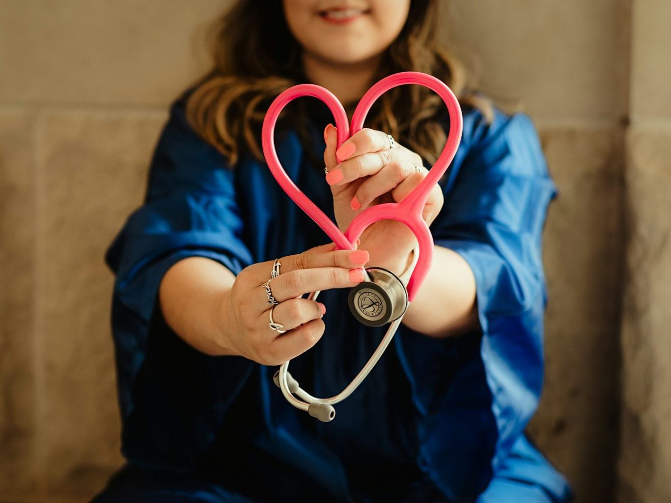 Doctor holding a pink stethoscope in a heart shape, smiling warmly.